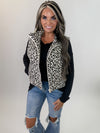 Woman wearing a leopard print vest over a black long-sleeve shirt and blue jeans on a white background